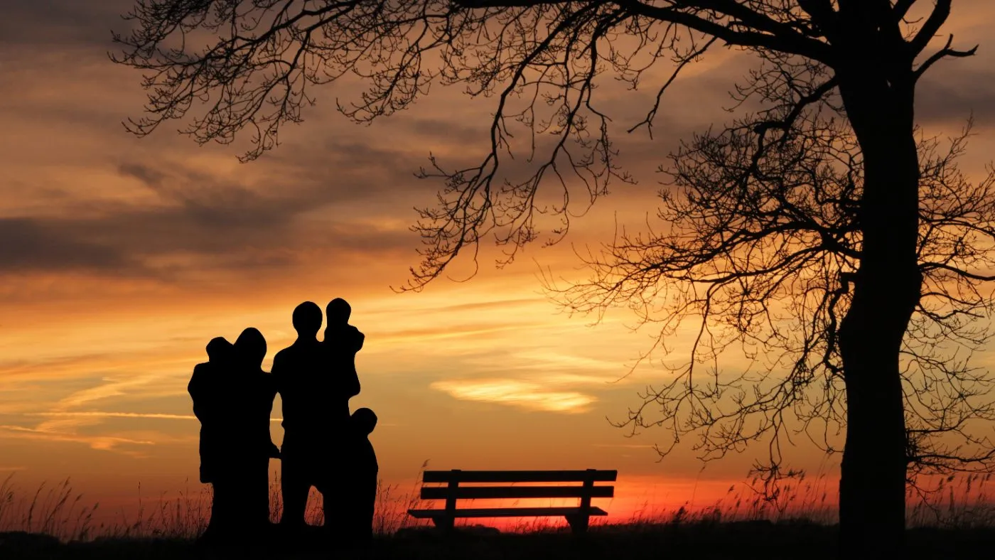 Família observando o pôr do sol sob uma árvore